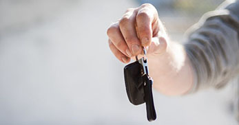 A hand holds a car key fob, with the background slightly blurred, suggesting an outdoor setting.